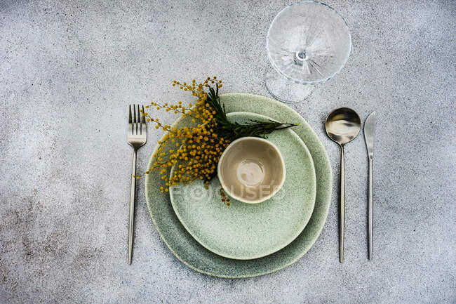 Configuração de mesa com flores de mimosa amarelo brilhante e utensílios de mesa cinza no fundo de concreto — Fotografia de Stock