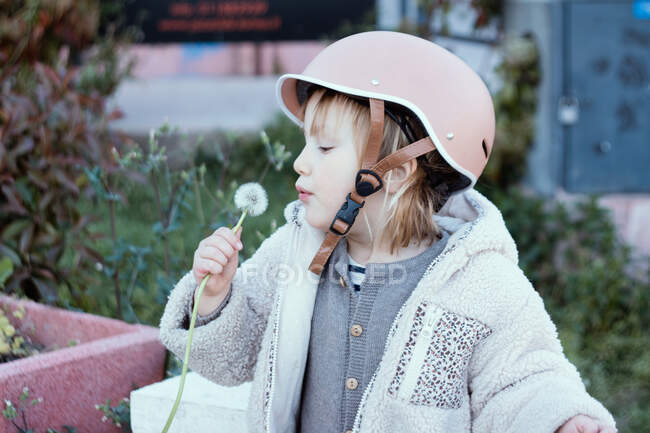 Little girl 4 years  in a helmet with a dandelion in her hand — Stock Photo