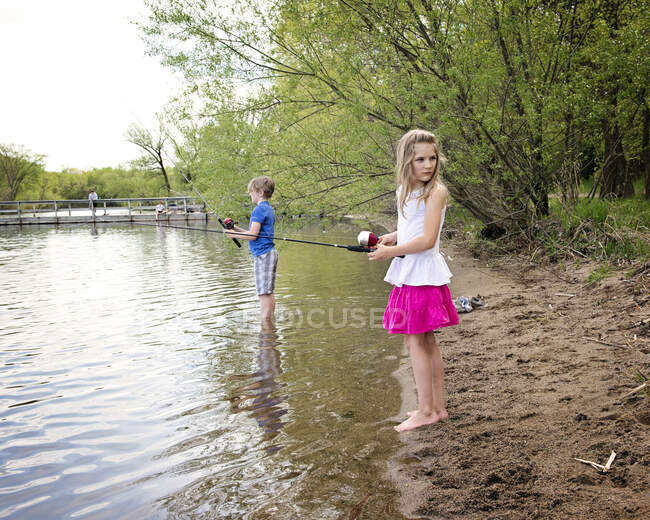 Девочка и мальчик ловят рыбу на берегу озера — стоковое фото