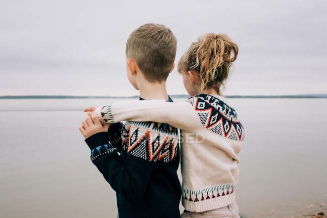 Brother and sister hugging looking out to sea on a cloudy day together — Stock Photo