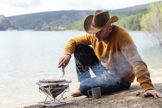 Uomo che prepara la carne vicino al lago — Foto stock
