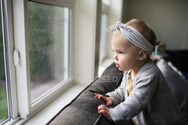 Pretty young girl looking out window from inside her home. — Stock Photo