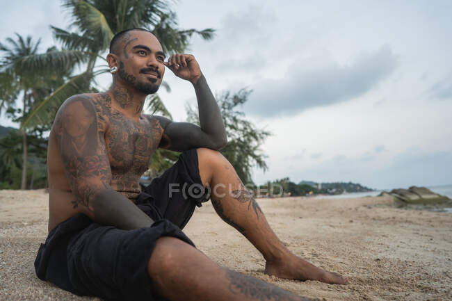 Asiatico ragazzo seduto su il spiaggia con un cane tra il palme — Foto stock