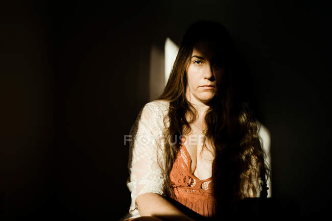 A woman sitting in the shadows wearing a red dress — Stock Photo