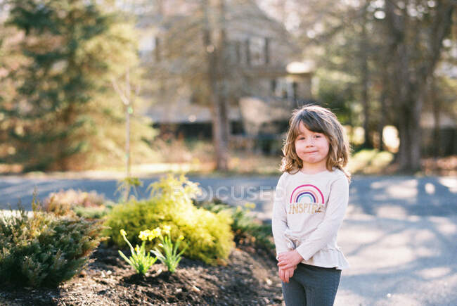 Petite fille debout dans son allée avec un large sourire pour la caméra — Photo de stock