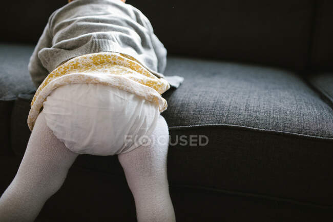 Detalle de una niña de un año subiendo al sofá - foto de stock