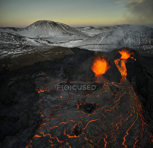 Живописный вид дрона на горячую оранжевую лаву, извергающуюся из вулканического кратера и протекающую вдоль скалистой земли — стоковое фото