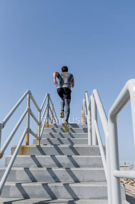 Junger Mann rennt bei klarem Himmel nach oben, trägt Sportbekleidung — Stockfoto
