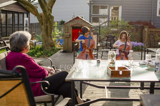 Two children give cello concert for grandmother at dinner table — Stock Photo