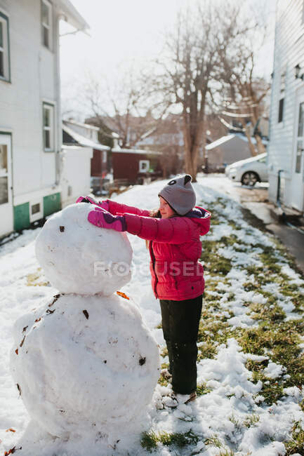 Giovane ragazza costruisce pupazzo di neve fuori mentre nevica — Foto stock