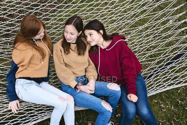 Three tween girls sitting on a hammock together talking. — Stock Photo