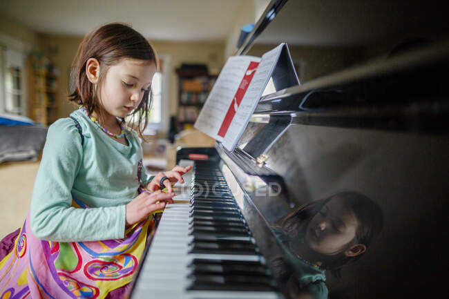 A little girl in butterfly wings sits at piano playing music indoors — Stock Photo