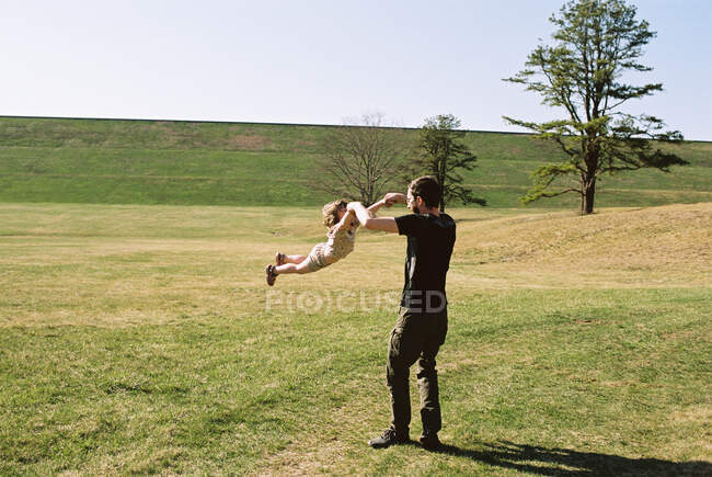 Uma menina e seu pai brincando em um campo gramado por um dique — Fotografia de Stock