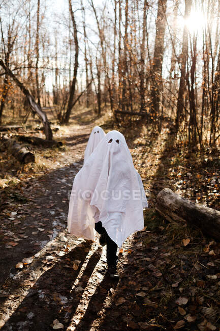 Due bambini in costume da fantasma che corrono in un parco in autunno — Foto stock
