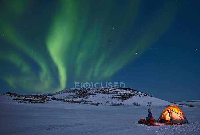 Frau sitzt außerhalb ihres Zeltes und blickt auf Nordlichter am Himmel — Stockfoto