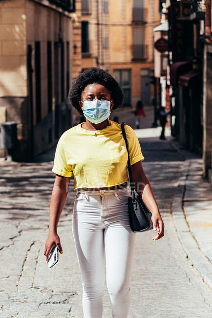 Afro-americano ragazza con maschera a piedi lungo una strada della città. — Foto stock