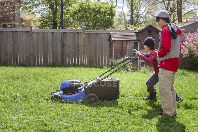 Мальчик стрижет газон ранней весной, пока отец присматривает за ним. — стоковое фото
