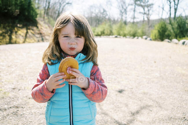 Une petite fille avec un visage prétendument méchant posant avec son beignet à la main — Photo de stock