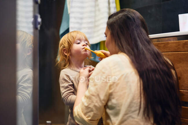 Beautiful woman brushes her teeth in the bathroom with her red-haired boy — Stock Photo