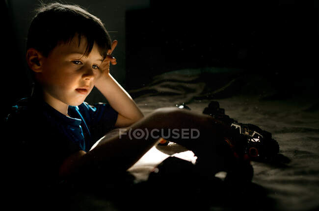 Мальчик в голубой рубашке играет с машинами на кровати в спальне — стоковое фото