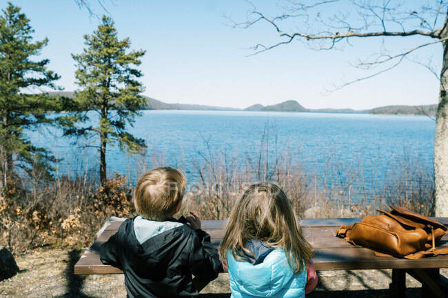 Duas crianças sentadas em um banco de piquenique com vista para um lago no nordeste — Fotografia de Stock