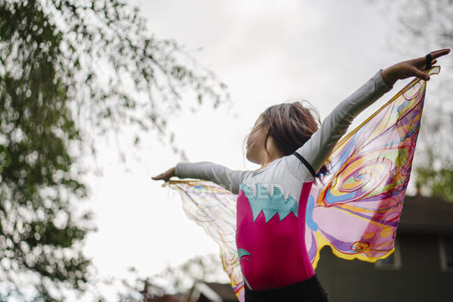 A little girl in transparent butterfly wings lifts arms towards sky — Stock Photo
