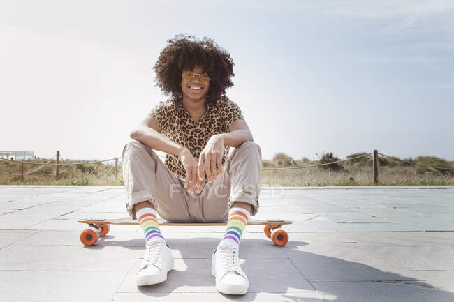 Afro Latino sitzt auf einem Longboard an der Strandpromenade — Stockfoto