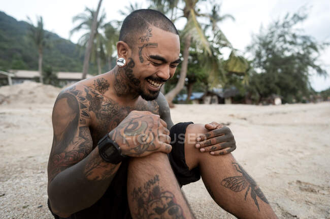 Hipster chico con tatuaje sentado en la playa en tailandia - foto de stock