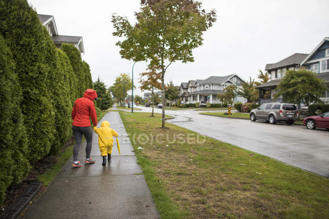 Madre cammina con figlio sul marciapiede durante una giornata piovosa. — Foto stock