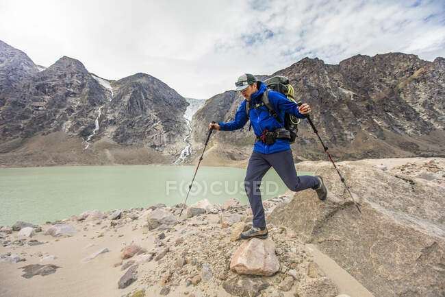 Backpacker hikes over boulders next to glacial fed lake. — Stock Photo