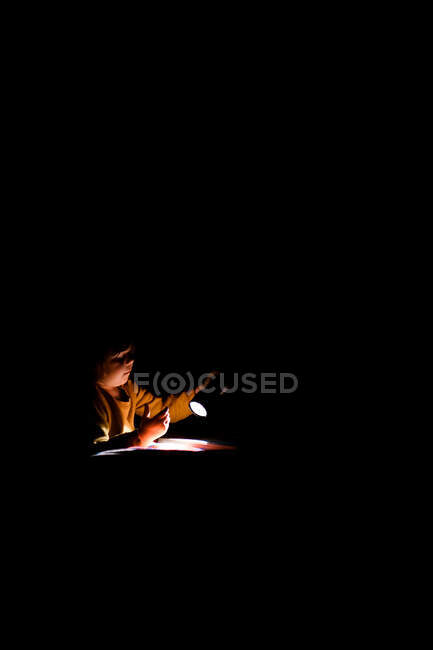 Дошкольница играет с фонариком на кровати в спальне — стоковое фото