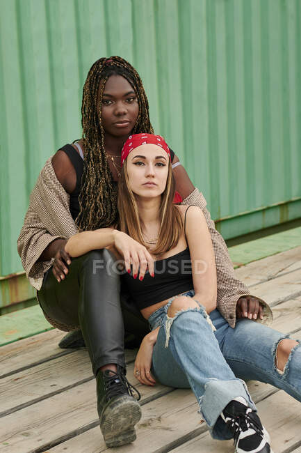 Mujeres multiétnicas abrazándose con ropa urbana posando frente a la cámara - foto de stock