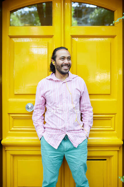 Усміхнений молодий іспаномовний чоловік слухає музику на барвистій вулиці — стокове фото