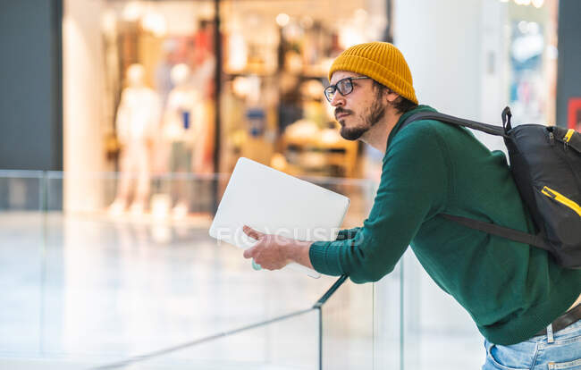 Homem espanhol moderno com óculos e laptop posando no shopping — Fotografia de Stock