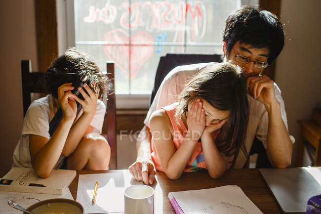 Due bambini infelici con la testa in mano siedono con il padre stanco a tavola — Foto stock