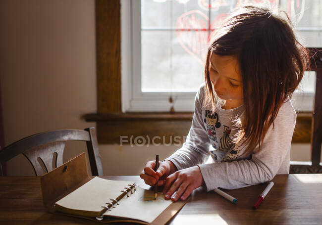 Uma menina pequena na luz bonita desenha em um diário couro-bound — Fotografia de Stock