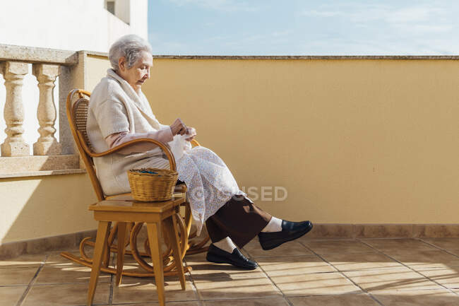 Пожилая женщина шитье с иголкой и ниткой на открытой террасе — стоковое фото