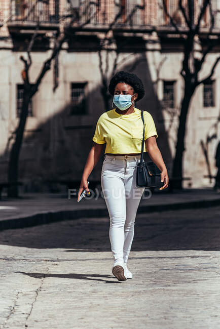 Афроамериканська дівчина з маскою обличчя йде по міській вулиці. — стокове фото