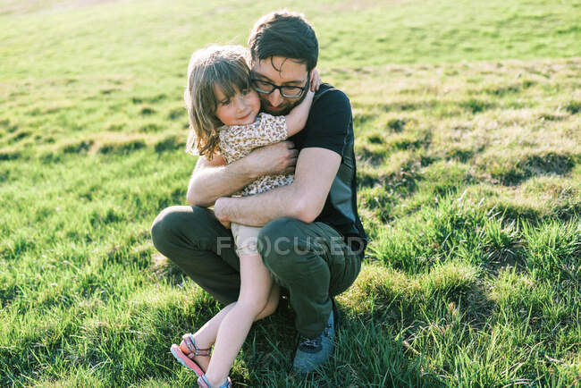 Feliz niña pequeña abrazando a su padre con gafas y sonriendo - foto de stock