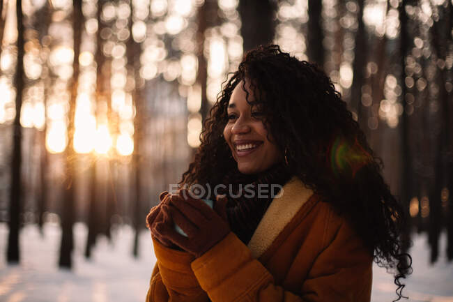 Joyeux jeune femme tenant une tasse de thé debout dans le parc pendant l'hiver — Photo de stock
