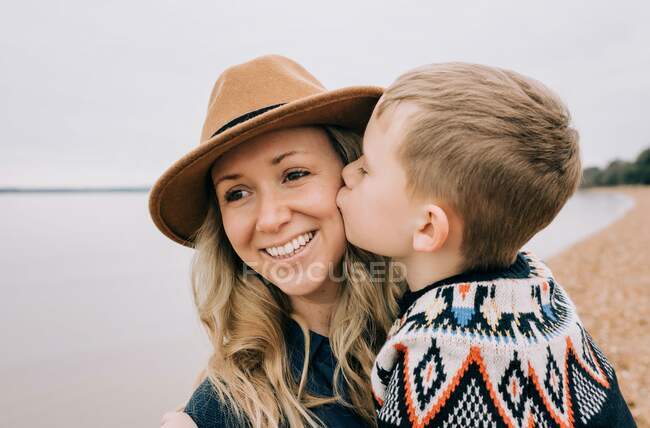 Hijo besando a sus mamás mejilla mientras en la playa felizmente jugando - foto de stock