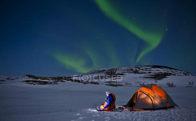 Wissenschaftlerin sitzt vor ihrem Zelt mit Nordlichtern am Himmel — Stockfoto
