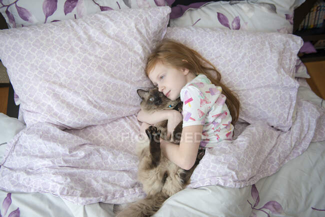 Больная маленькая девочка обнимает кошку в постели — стоковое фото