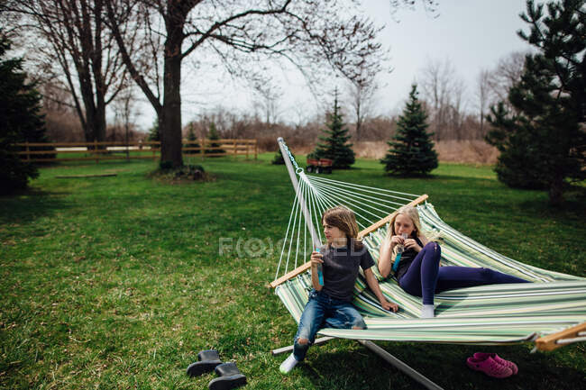 Мальчик и девочка отдыхают на гамаке во дворе весной — стоковое фото