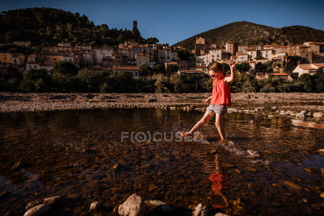 Девушка брызгает водой в реке во Франции с деревней в фоновом режиме — стоковое фото