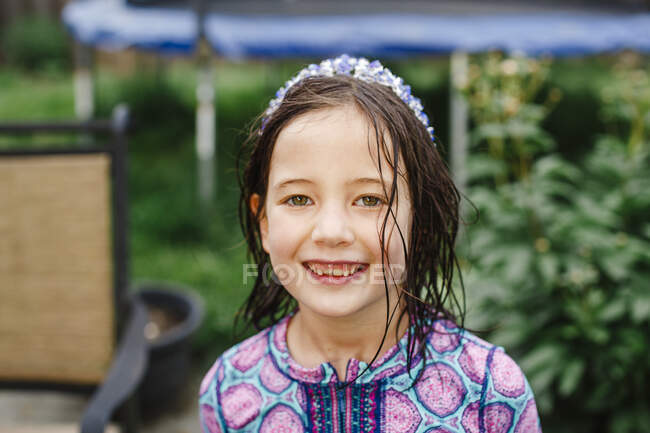 A smiling child stands with direct gaze, wet hair, and a purple crown — Stock Photo