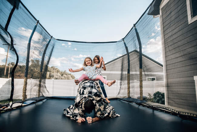 Дочери играют с отцом на батуте летом — стоковое фото