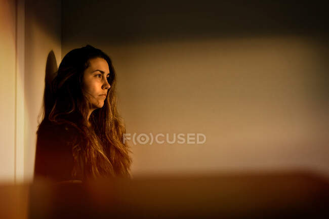 Una mujer de pie en un dormitorio mirando el atardecer desde su ventana - foto de stock
