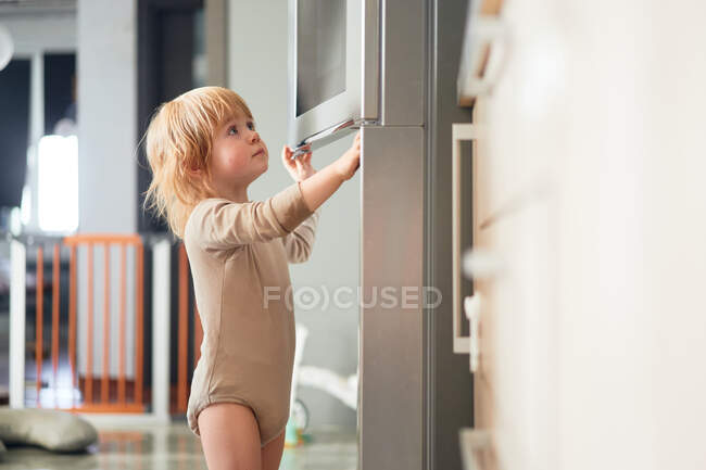 Рыжеволосый ребенок смотрит в холодильник. в поисках пищи — стоковое фото