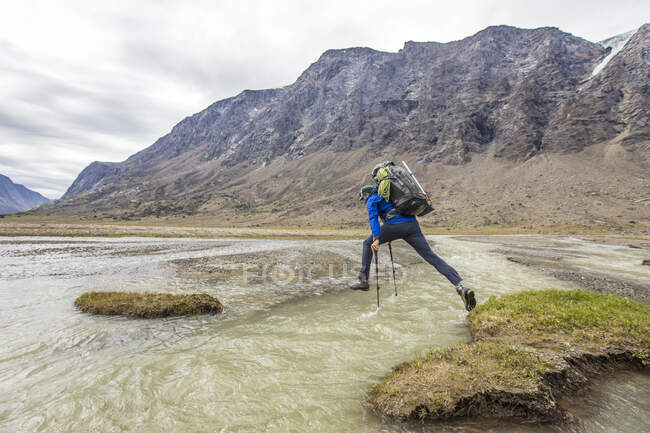Backpacker springt mit Trekkingstöcken über tiefen Flusskanal — Stockfoto